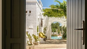 An open doorway leading to a courtyard with a pool, white buildings, and greenery. - Masseria Narducci (Fasano)