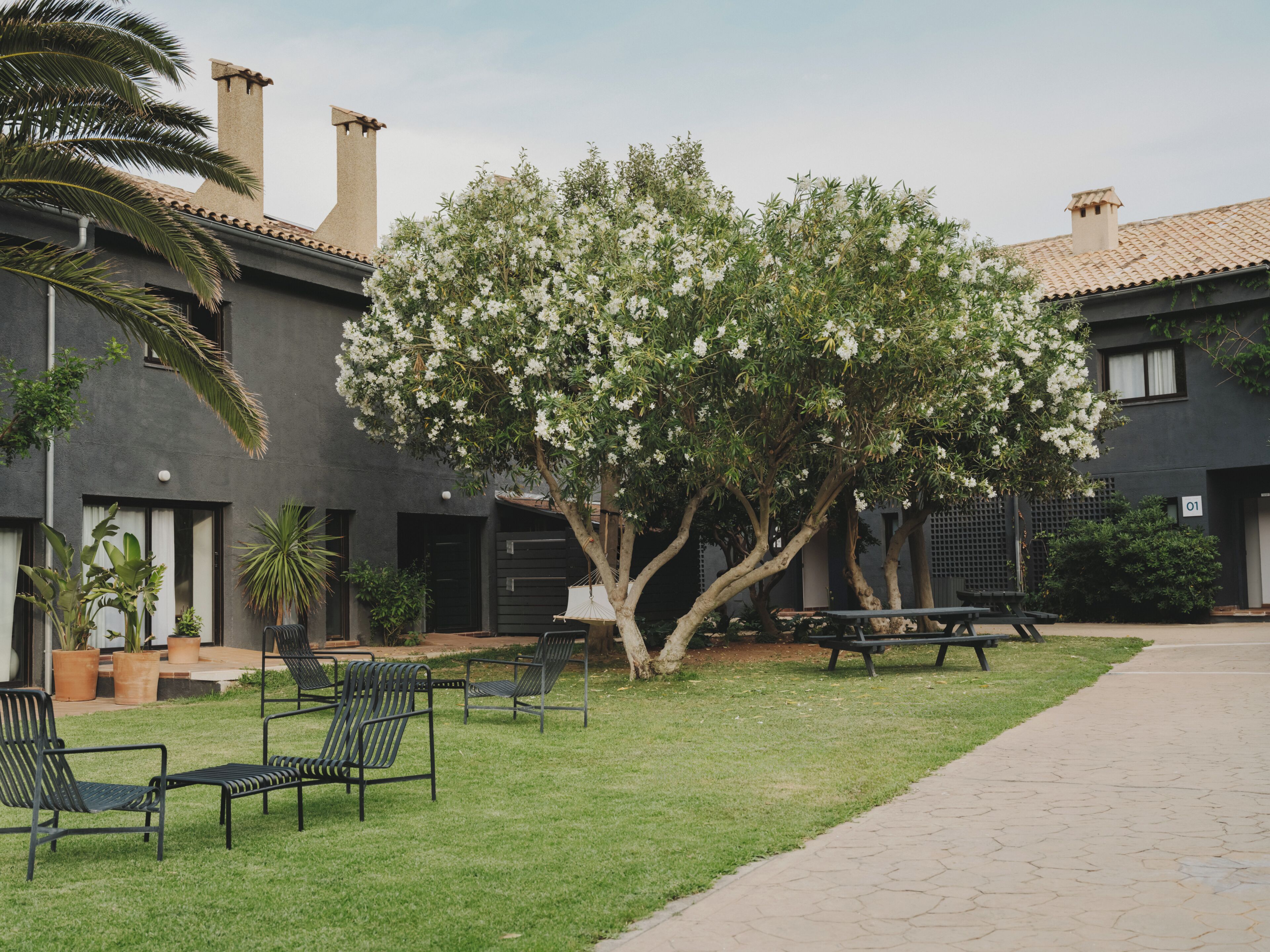 Un patio con un árbol, mesas al aire libre y un edificio de techo con tejas.