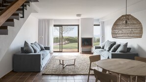 Una sala moderna con un sofá, una mesa redonda de centro, una mesa de comedor con sillas, una chimenea y vistas al exterior.