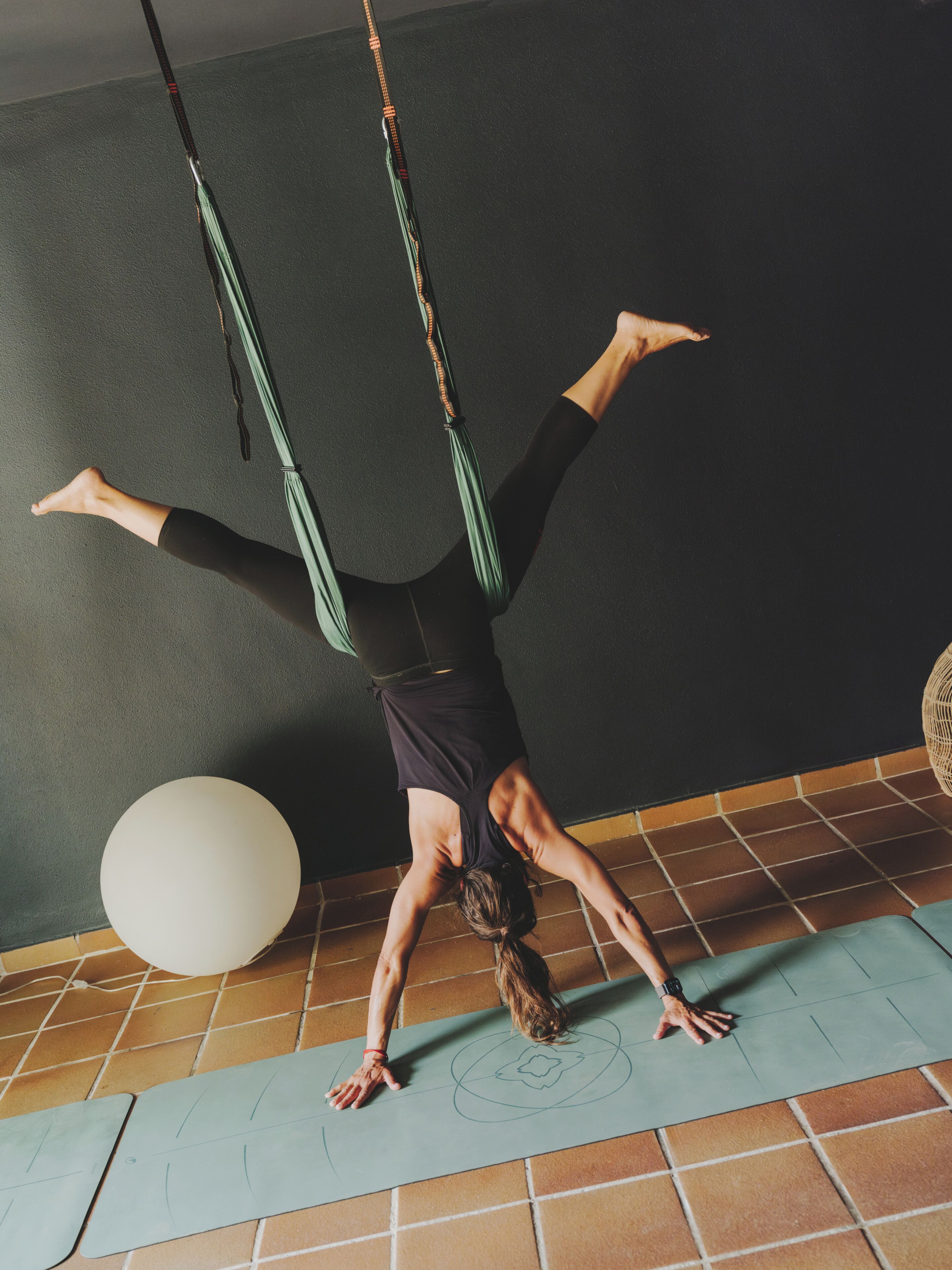 A person performing an aerial yoga pose with a yoga mat and a large exercise ball on the floor.