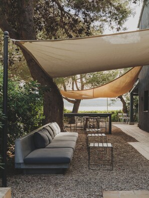 Un espace extérieur aménagé, abrité et doté de canapés et de tables, entouré d’arbres et offrant une vue sur le paysage.