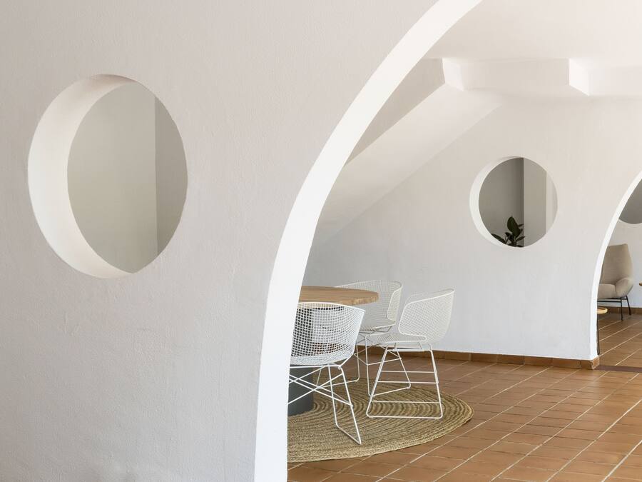 Un interior moderno con paredes blancas, círculos recortados, una mesa de madera y sillas de estructura metálica.