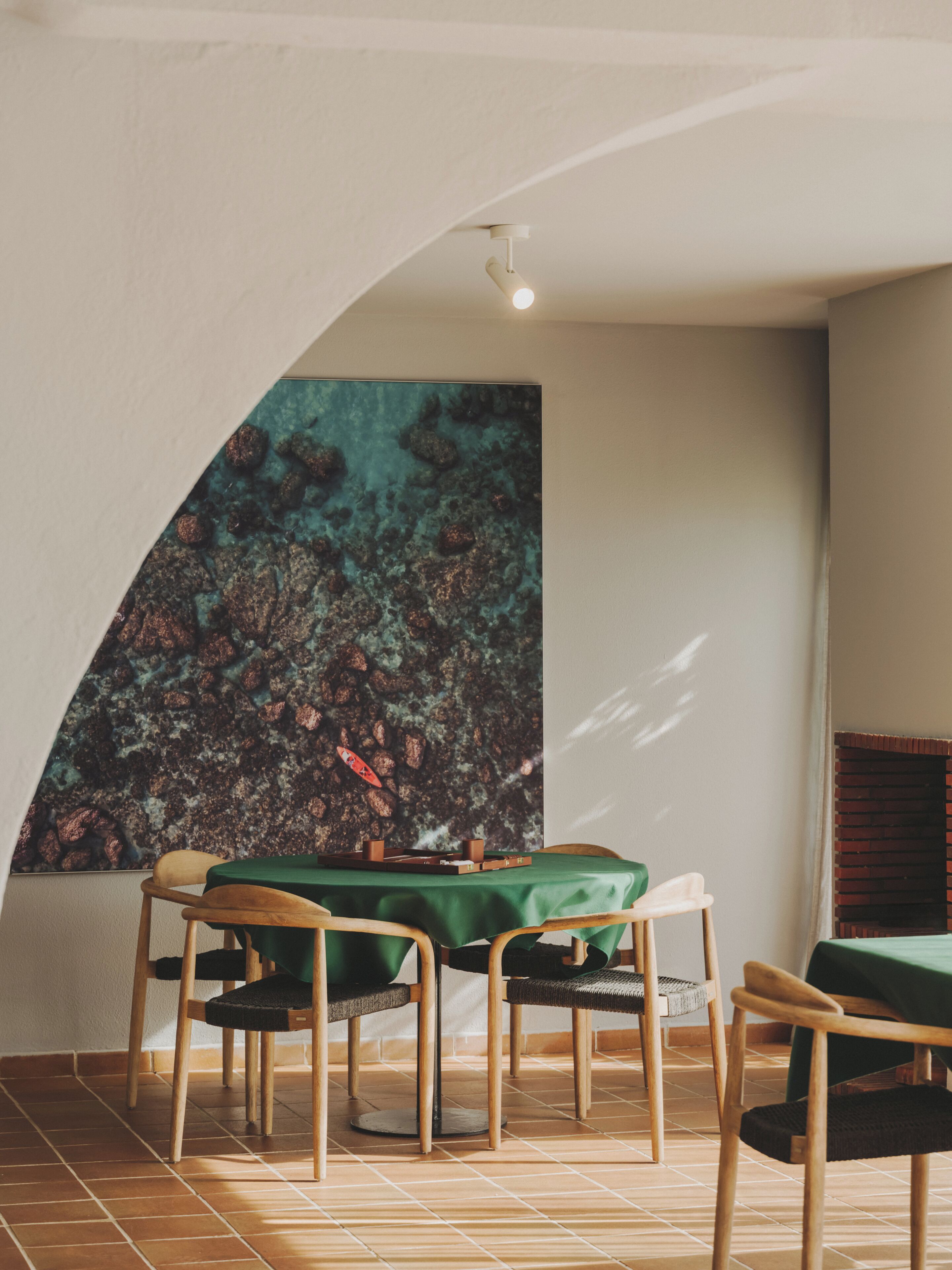 A dining area with a table set for two, chairs, and a wall with a large abstract painting.