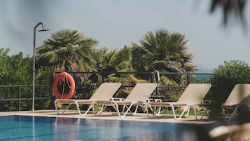 Un área junto a la piscina con sillones de descanso, un flotador salvavidas y palmeras.