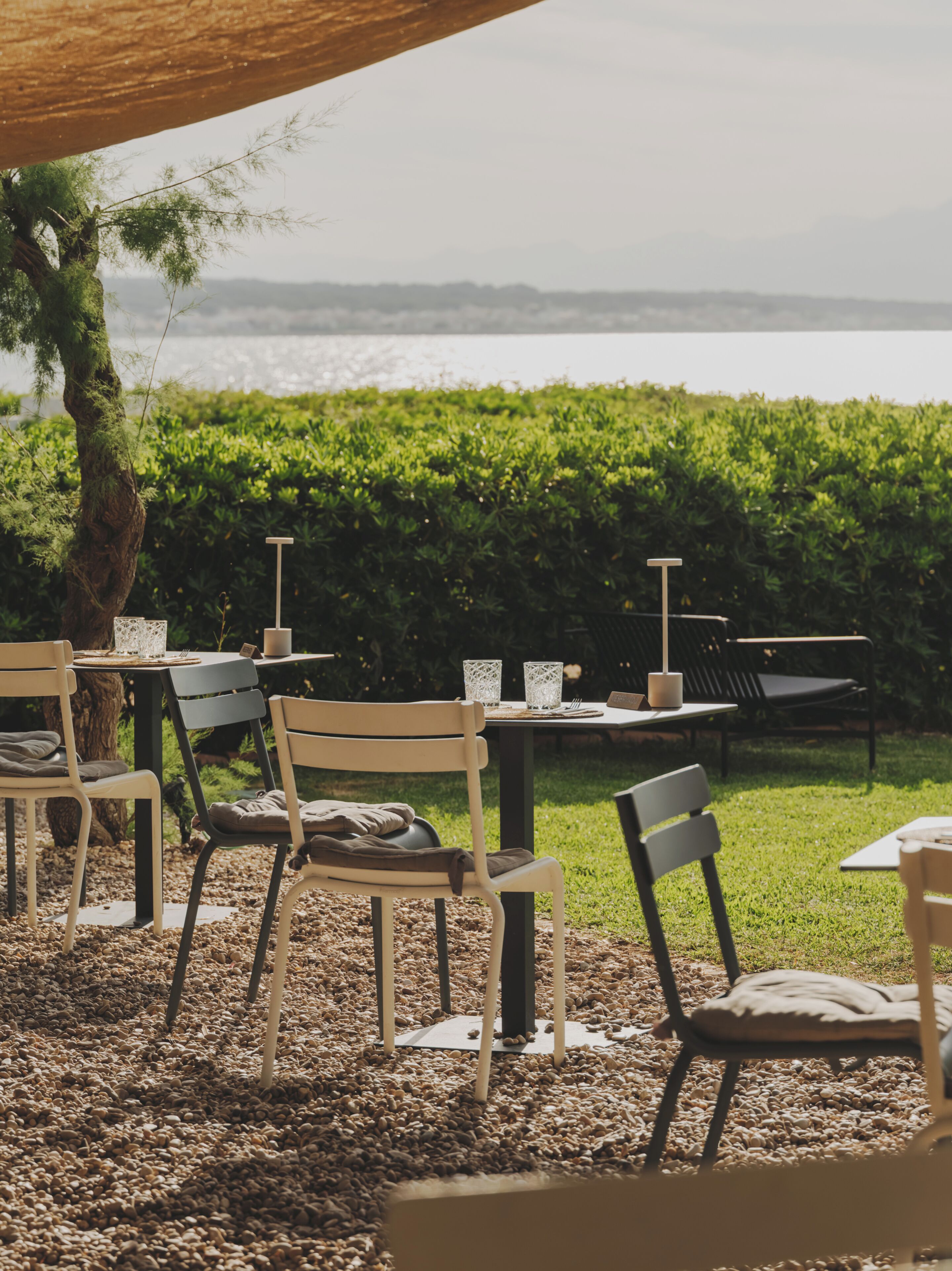 Een terras met tafels en stoelen, een uitzicht op zee en een haag op de achtergrond.