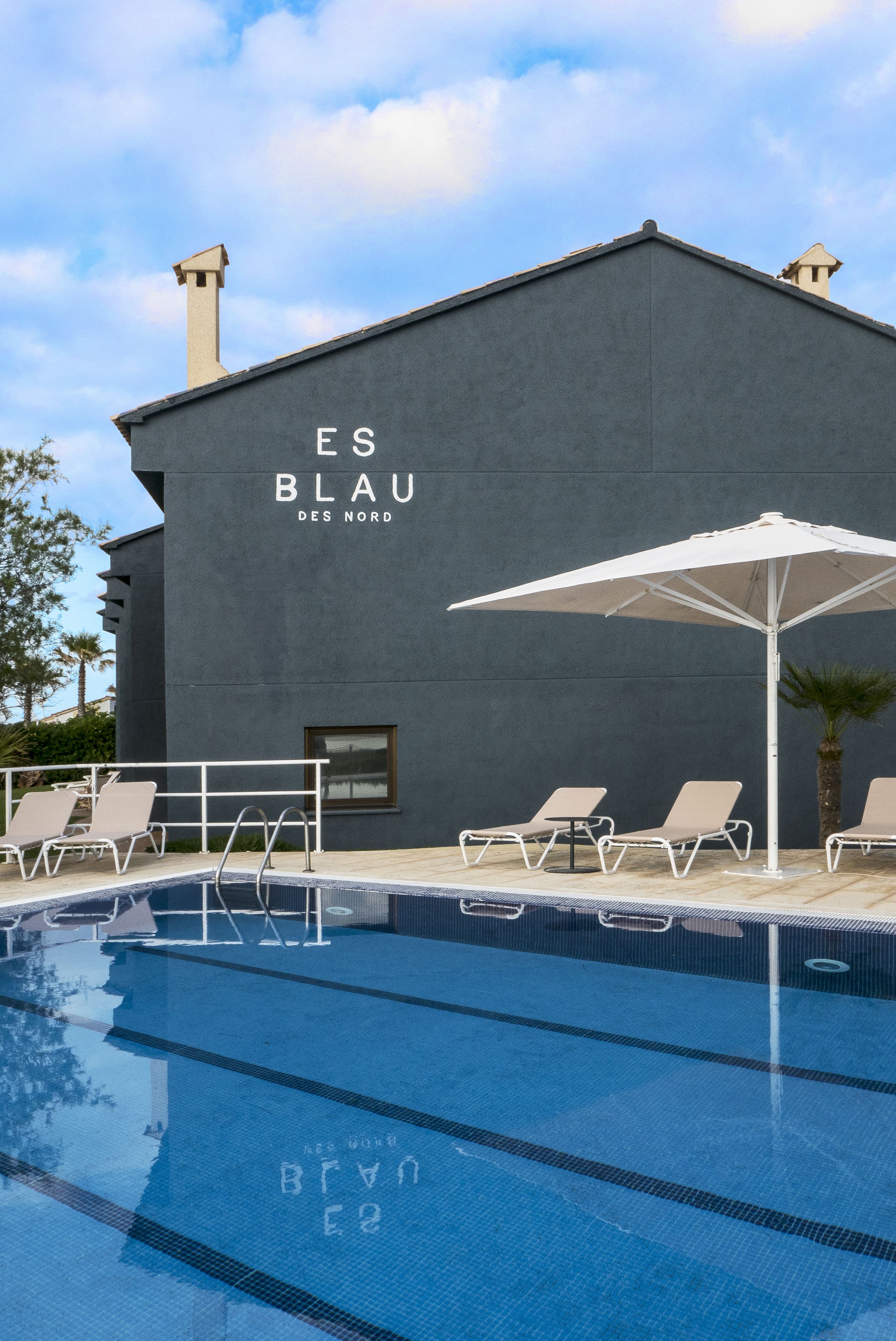 Un edificio moderno con piscina, sillas de descanso y sombrillas.