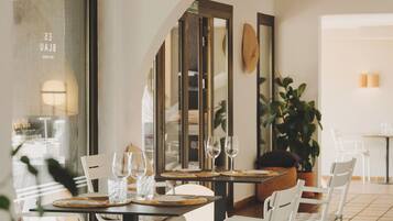 Un comedor con una mesa dispuesta para dos personas, sillas blancas y un espejo grande en la pared.