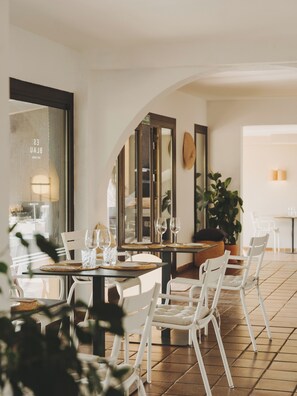 Un coin repas avec une table dressée pour deux personnes, des chaises blanches et un grand miroir au mur.