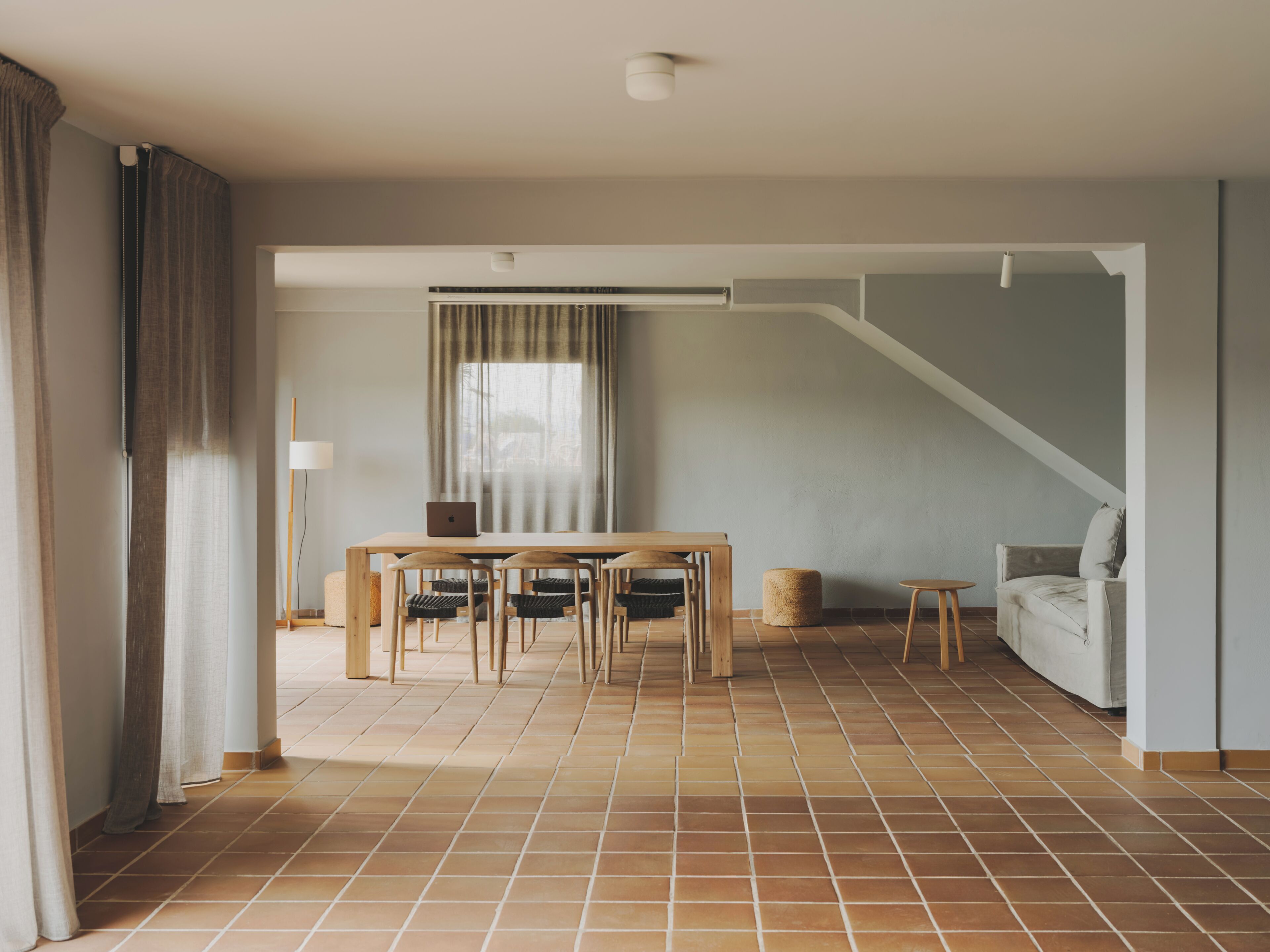 A spacious room with a dining table, chairs, a sofa, and a staircase.