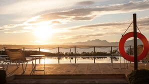 Vista del atardecer sobre un cuerpo de agua tranquilo con piscina, sillas y un adorno circular rojo.
