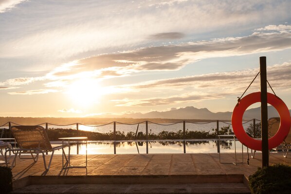 A sunset view over a calm body of water with a pool, chairs, and a red circular decoration. - Hotel Es Blau des Nord (Arta)