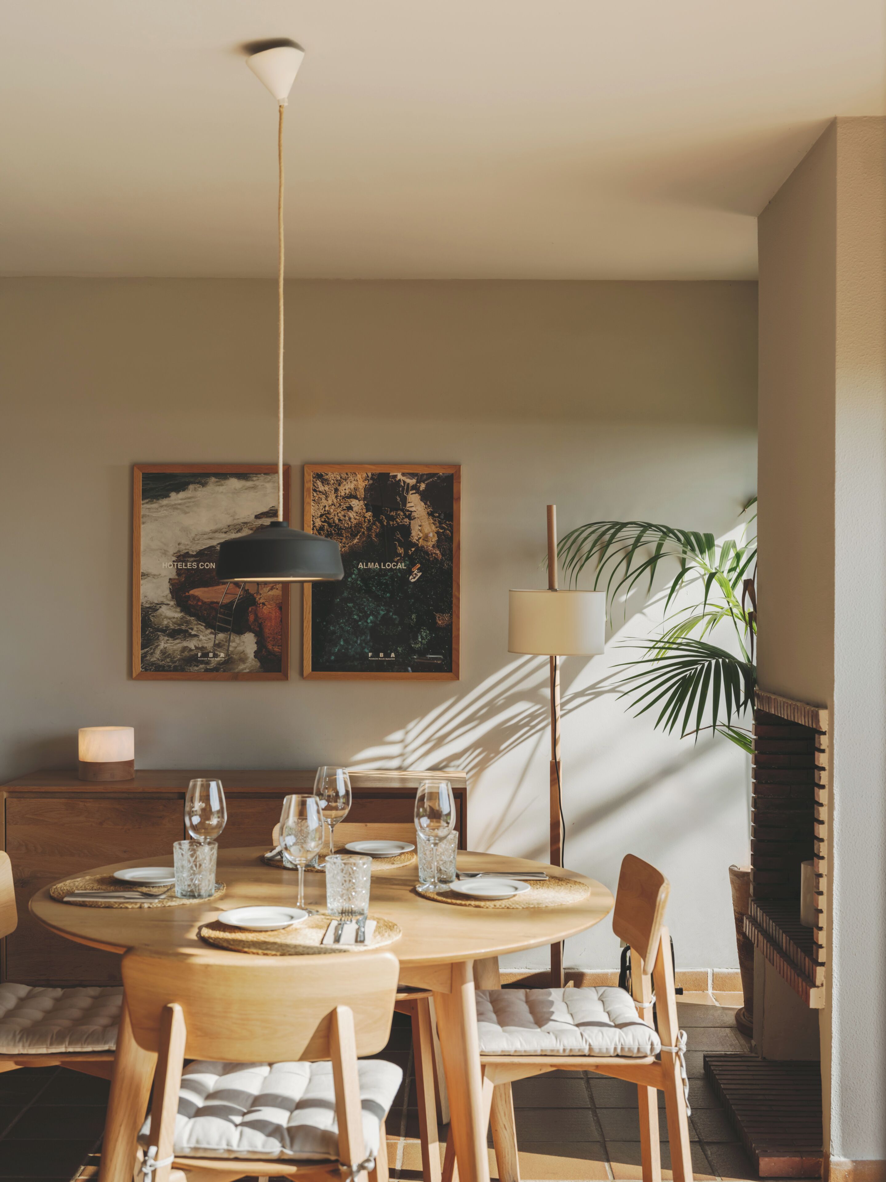 Un comedor con una mesa redonda dispuesta para cuatro personas, dos obras de arte colgadas en la pared, una lámpara de pie y una planta en maceta.