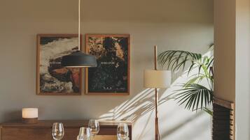 Un comedor con una mesa redonda dispuesta para cuatro personas, dos obras de arte colgadas en la pared, una lámpara de pie y una planta en maceta.