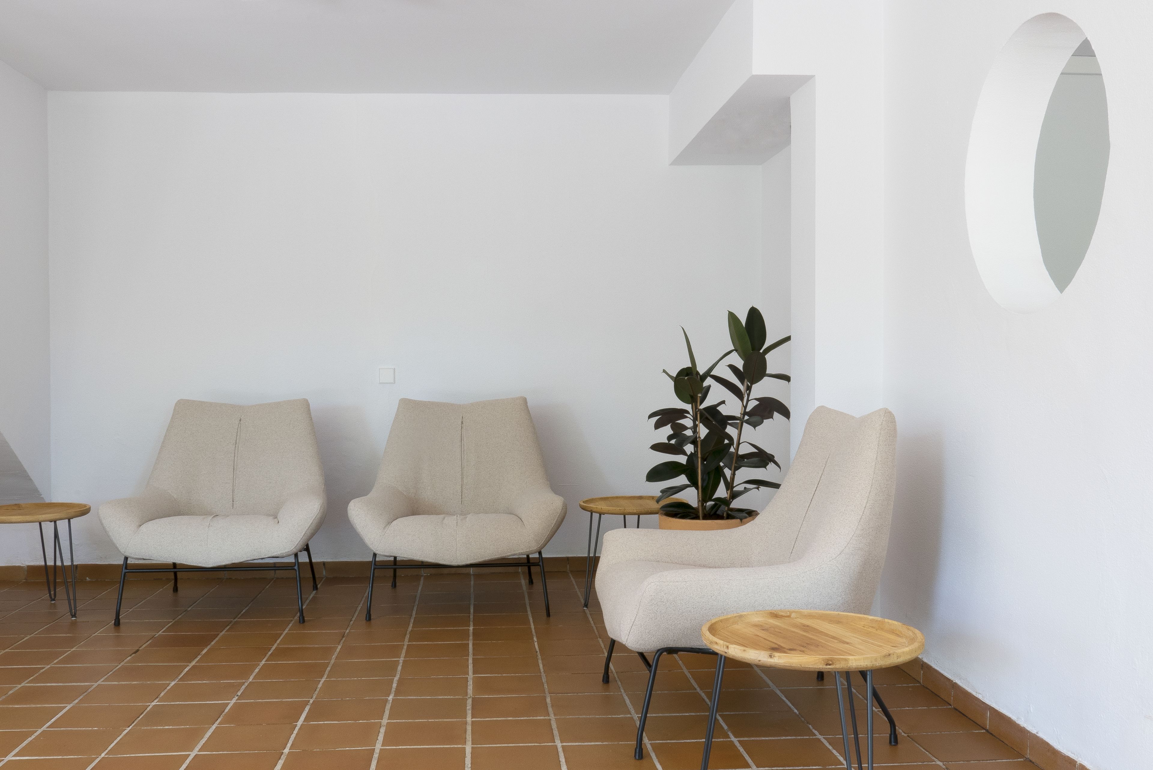 Une pièce comprenant trois fauteuils beiges, une plante en pot et deux petites tables en bois.