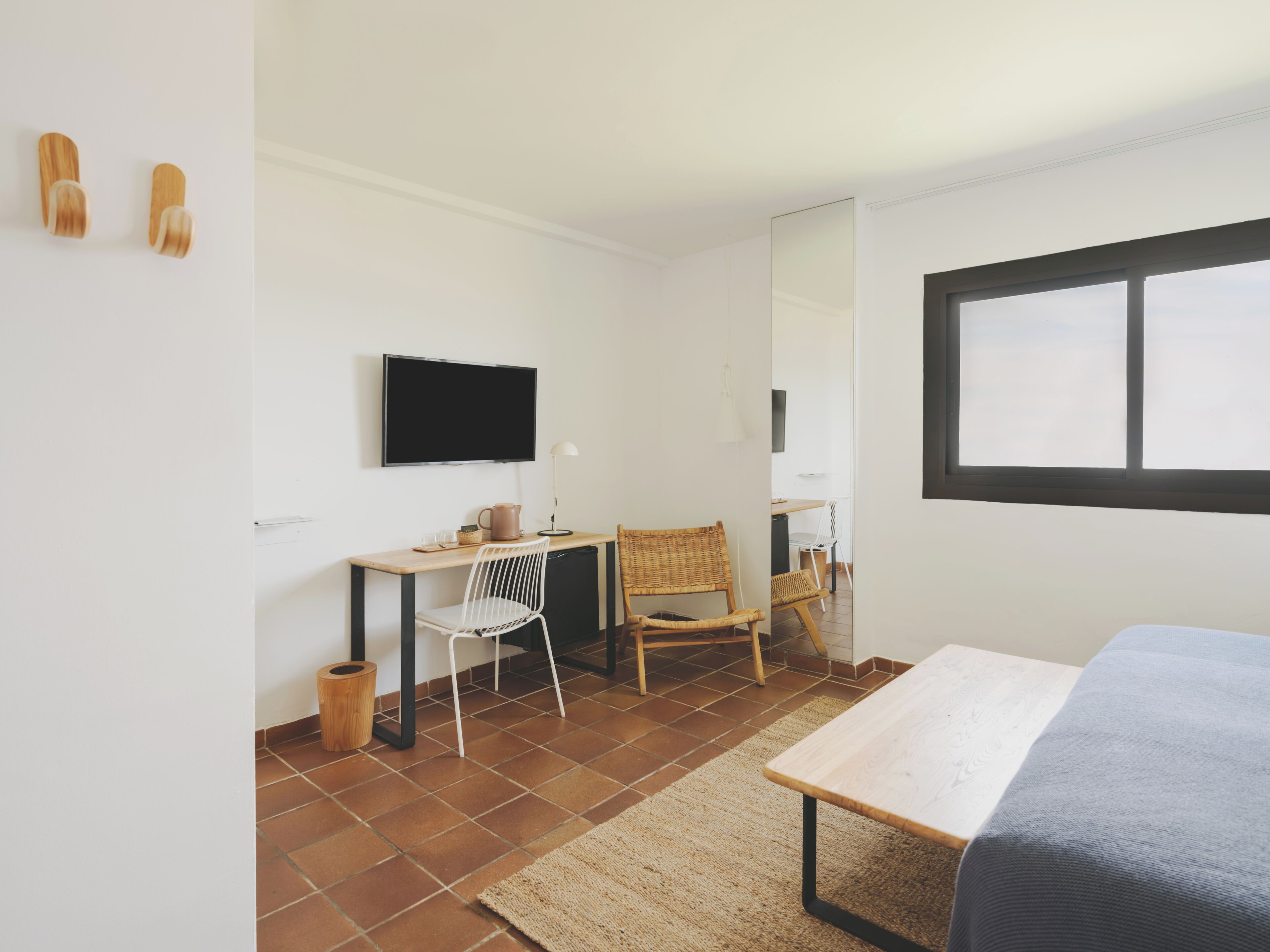 Een kamer met een bed, een bureau, twee stoelen, een televisie en een raam.