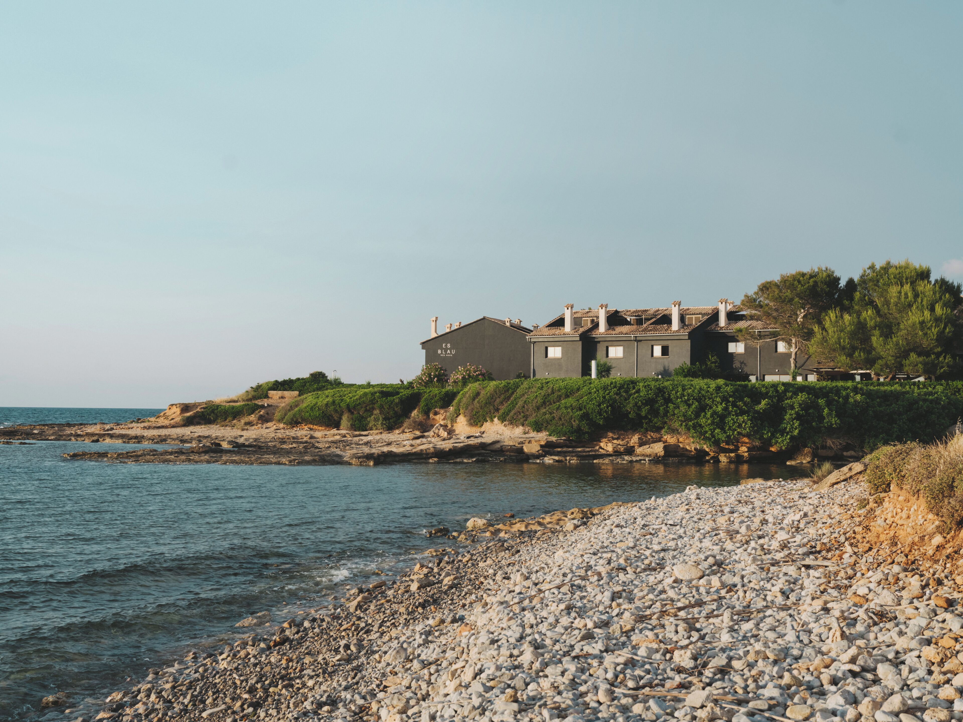 Propiedad costera con un edificio grande, costa rocosa y vegetación.