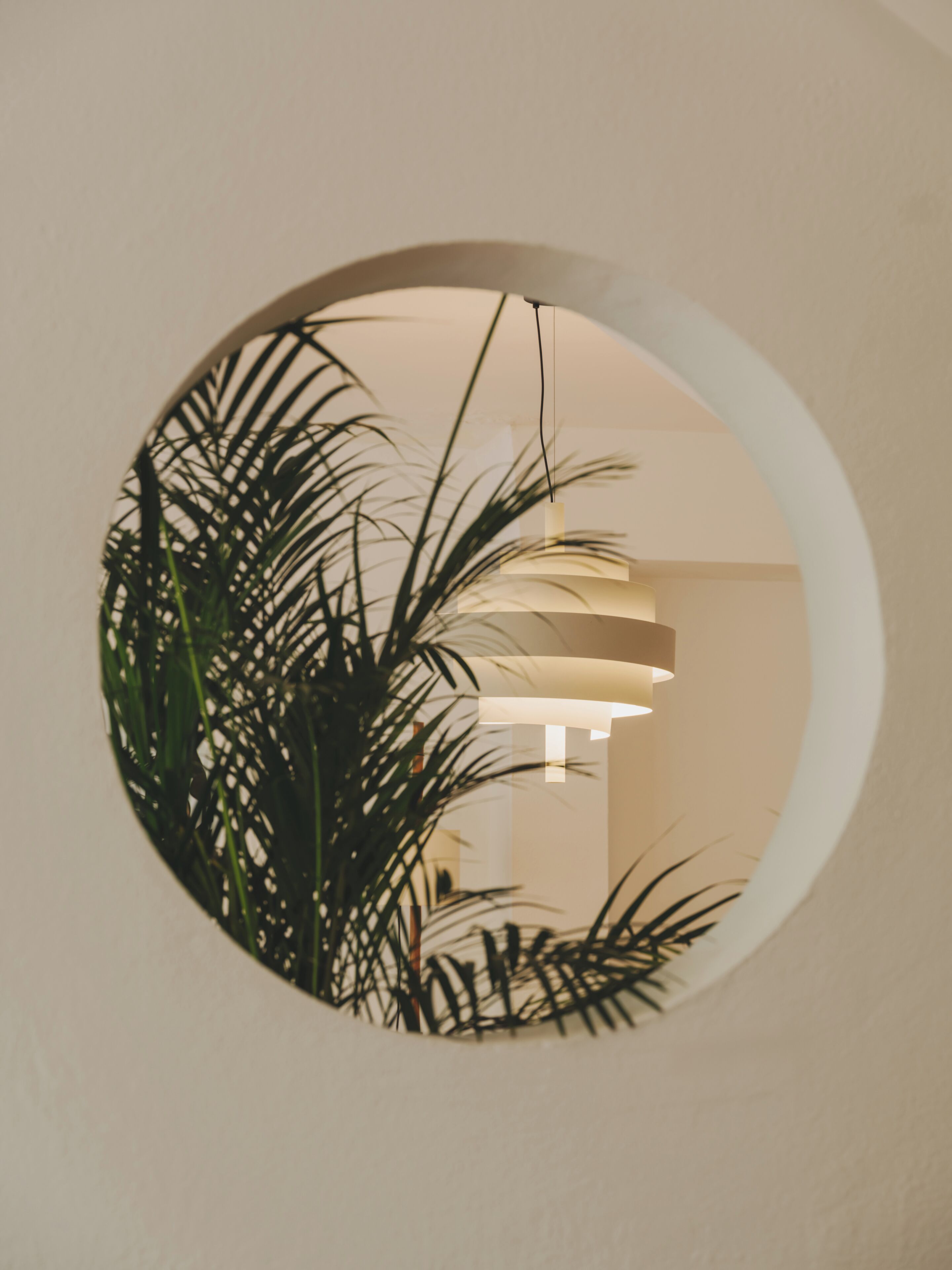Ein rundes Fenster mit Blick in einen Innenraum, inklusive Pflanze und einer Pendelleuchte.