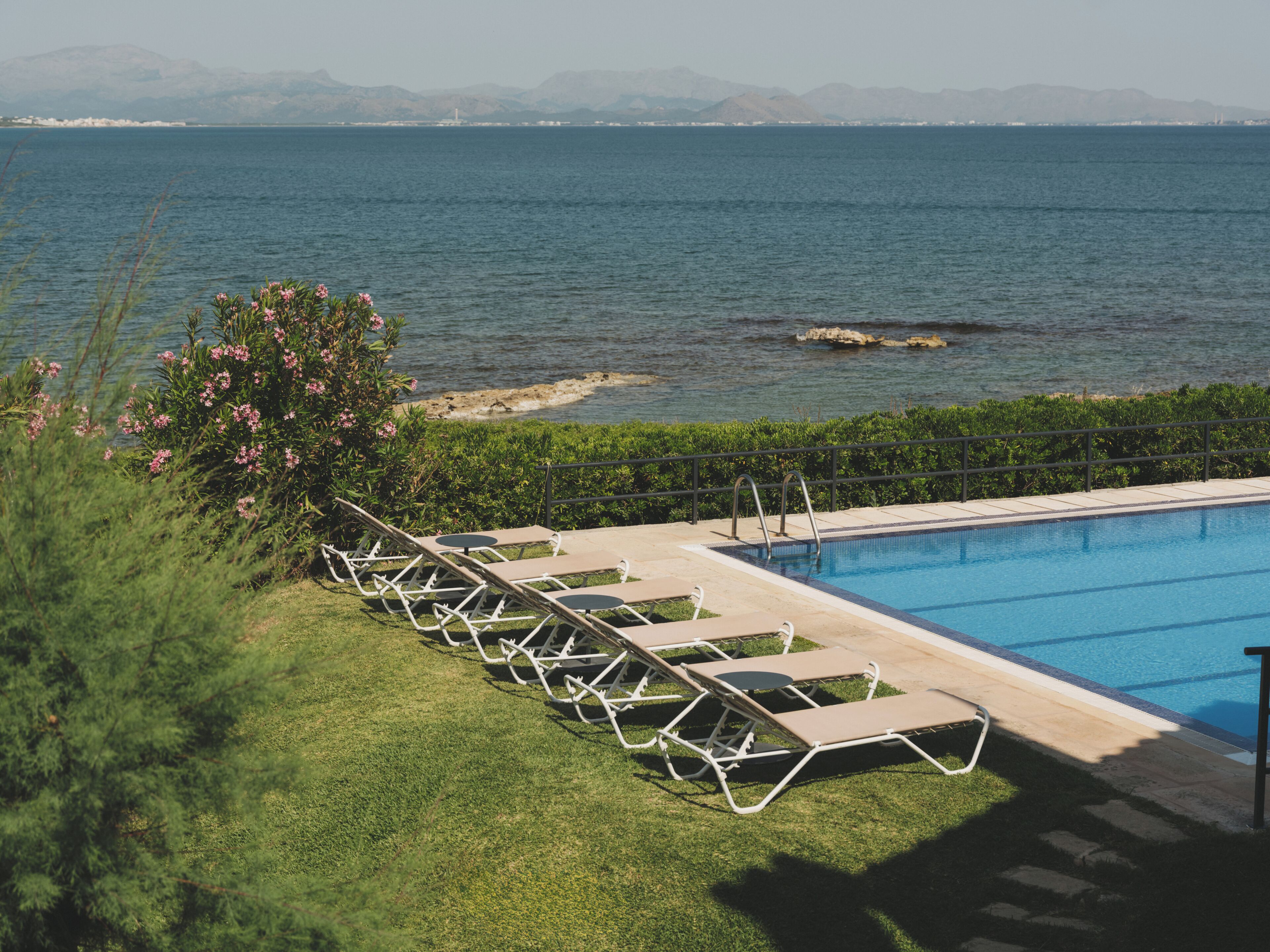 Zona de piscina con sillones de descanso y vista al mar.