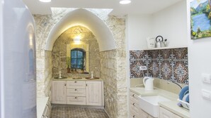 Un baño con un arco de piedra, suelo de baldosas y un lavabo con hervidor.