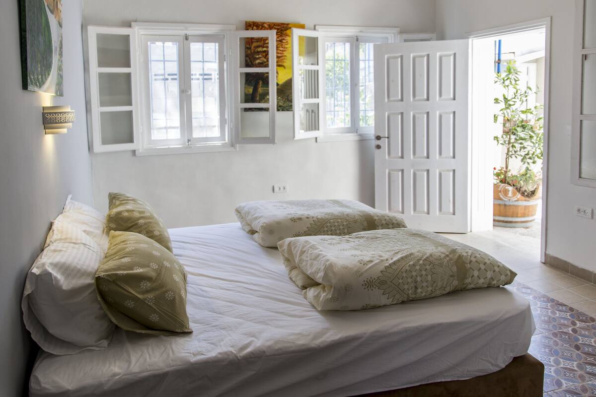A bedroom with a bed, pillows, a wardrobe with open doors, and a potted plant.