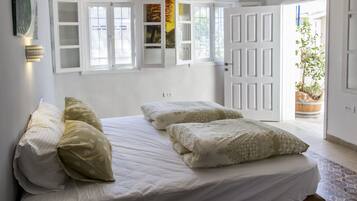 A bedroom with a bed, pillows, a wardrobe with open doors, and a potted plant.