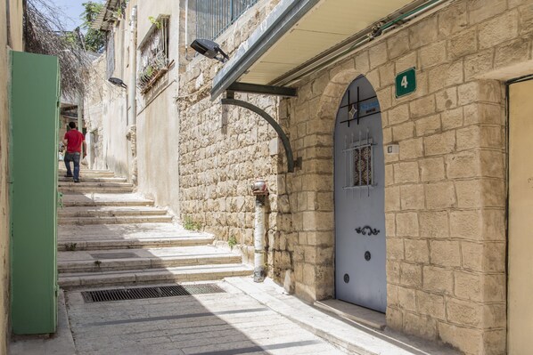 Una calle estrecha con edificios de piedra, un cartel visible con el número 4 y una persona alejándose.