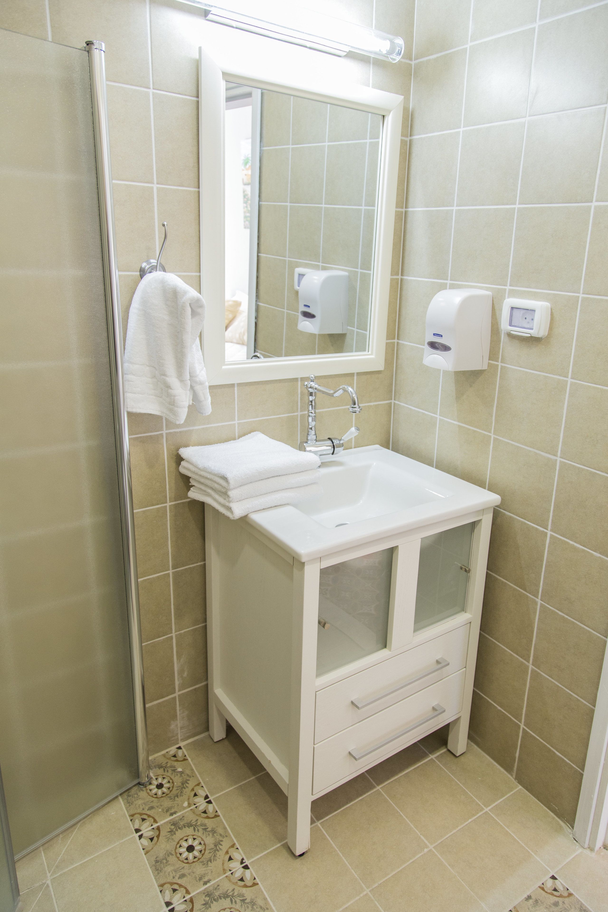 A bathroom with a white sink, a mirror, a towel rack, and a soap dispenser.