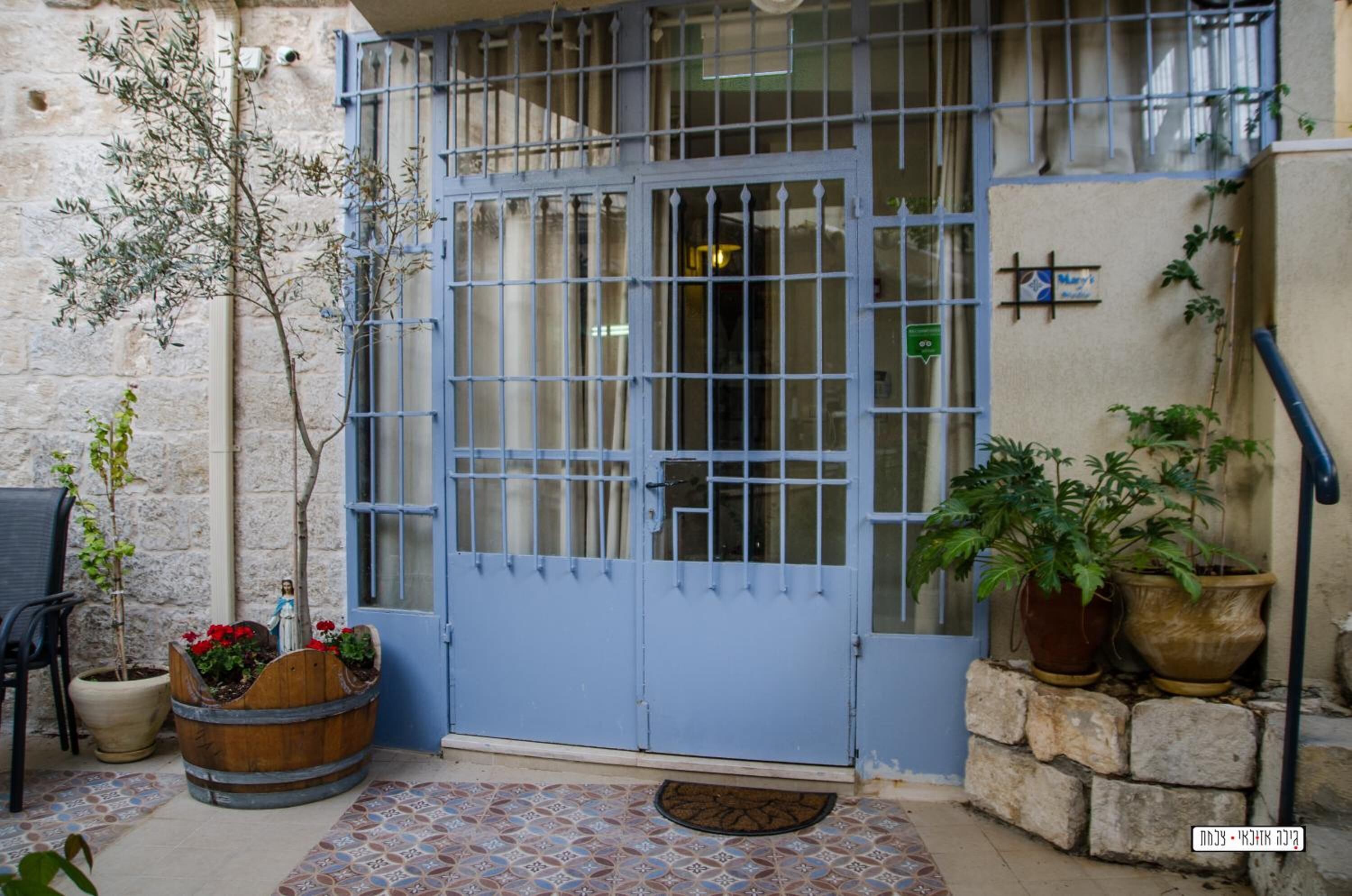 A blue gate with a small window, a potted plant with red flowers, and a tiled floor.