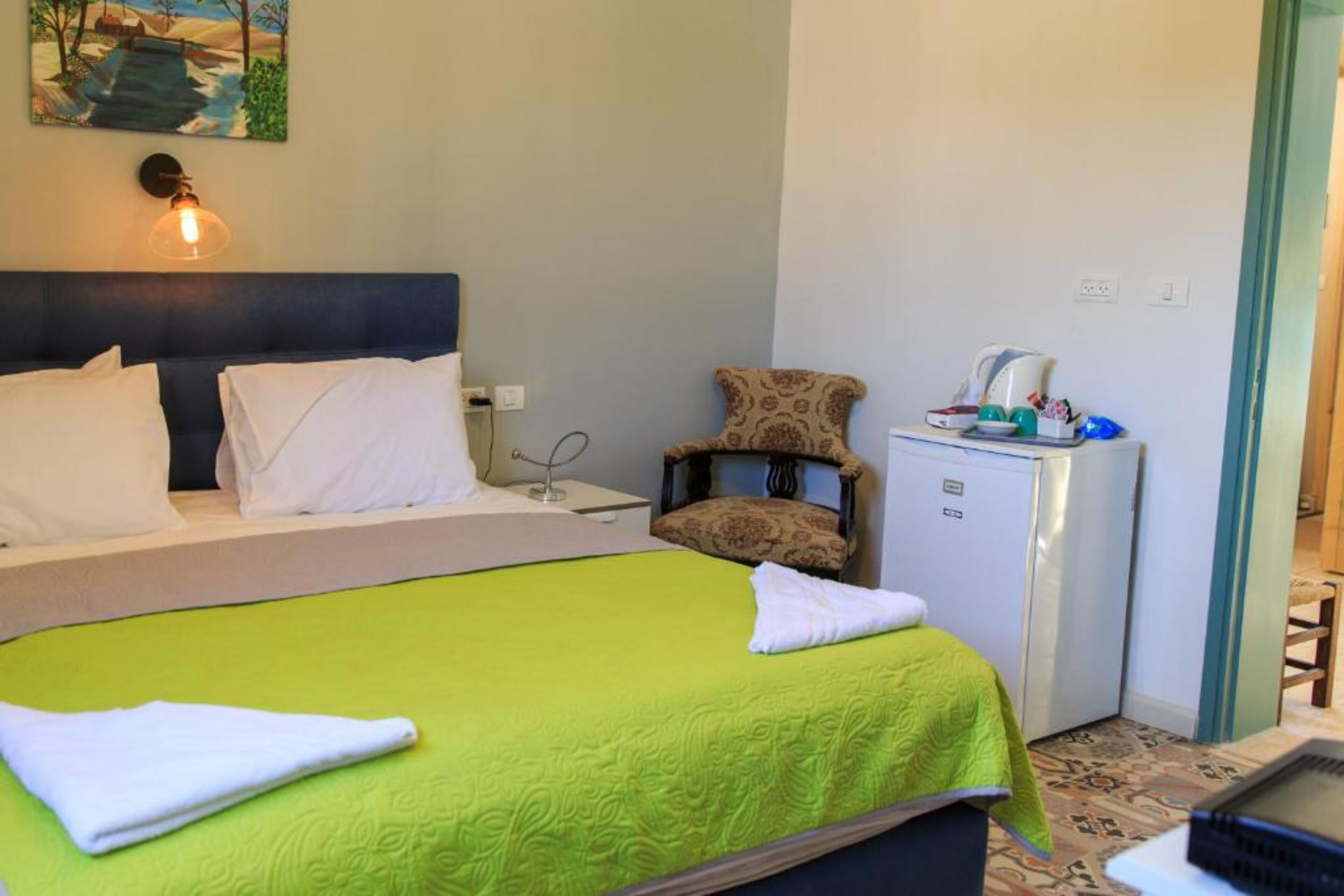 Una habitación de hotel con cama, una silla, un refrigerador pequeño y una mesa con una computadora portátil.