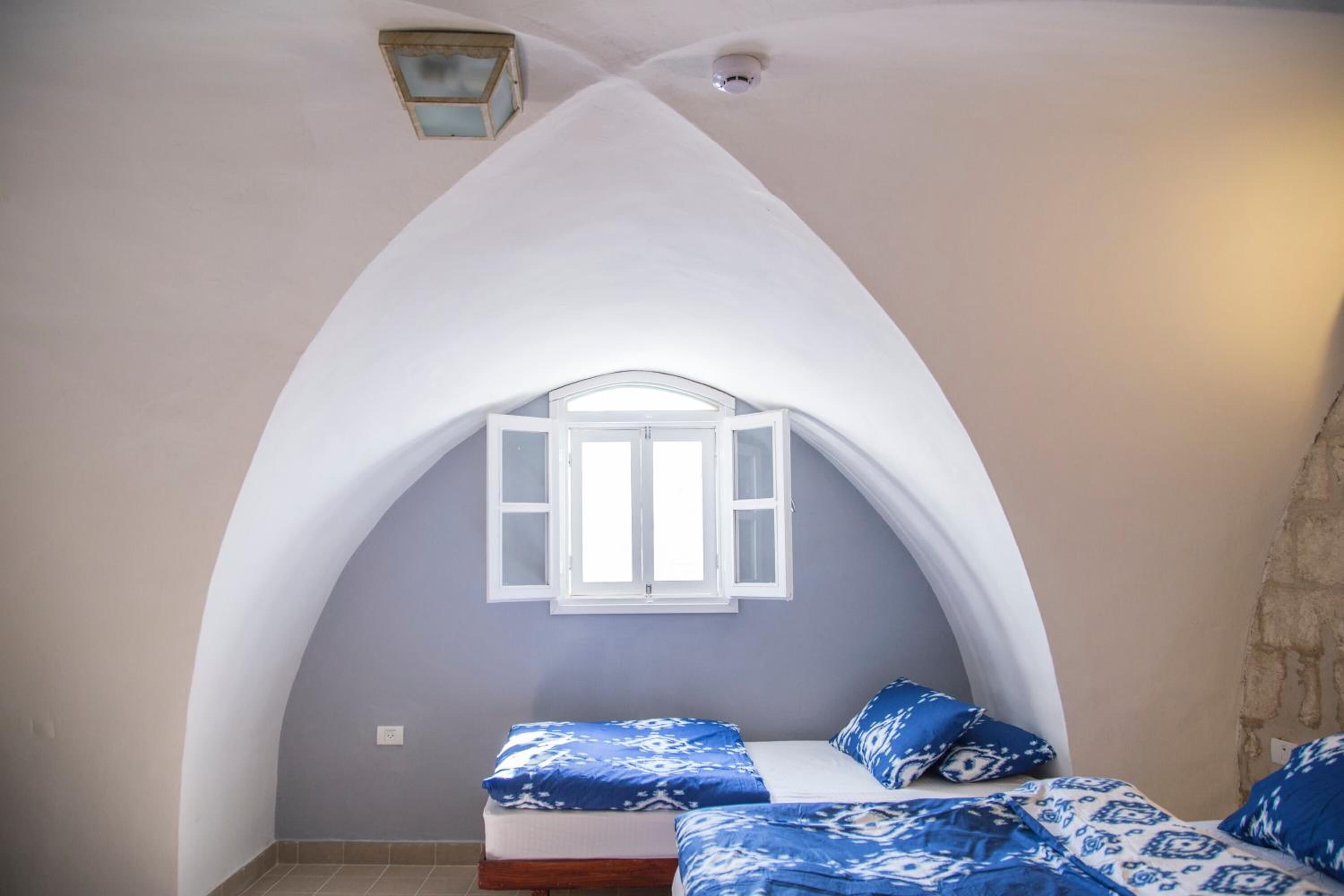 A bedroom with a vaulted ceiling, a window with white shutters, and a bed with blue patterned bedding.