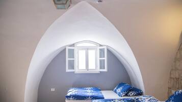 A bedroom with a vaulted ceiling, a window with white shutters, and a bed with blue patterned bedding.