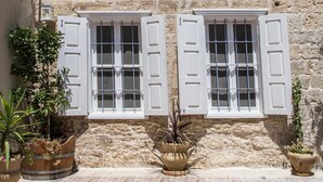 Un edificio de piedra con dos ventanas, cada una con contraventanas blancas, y un patio empinado.