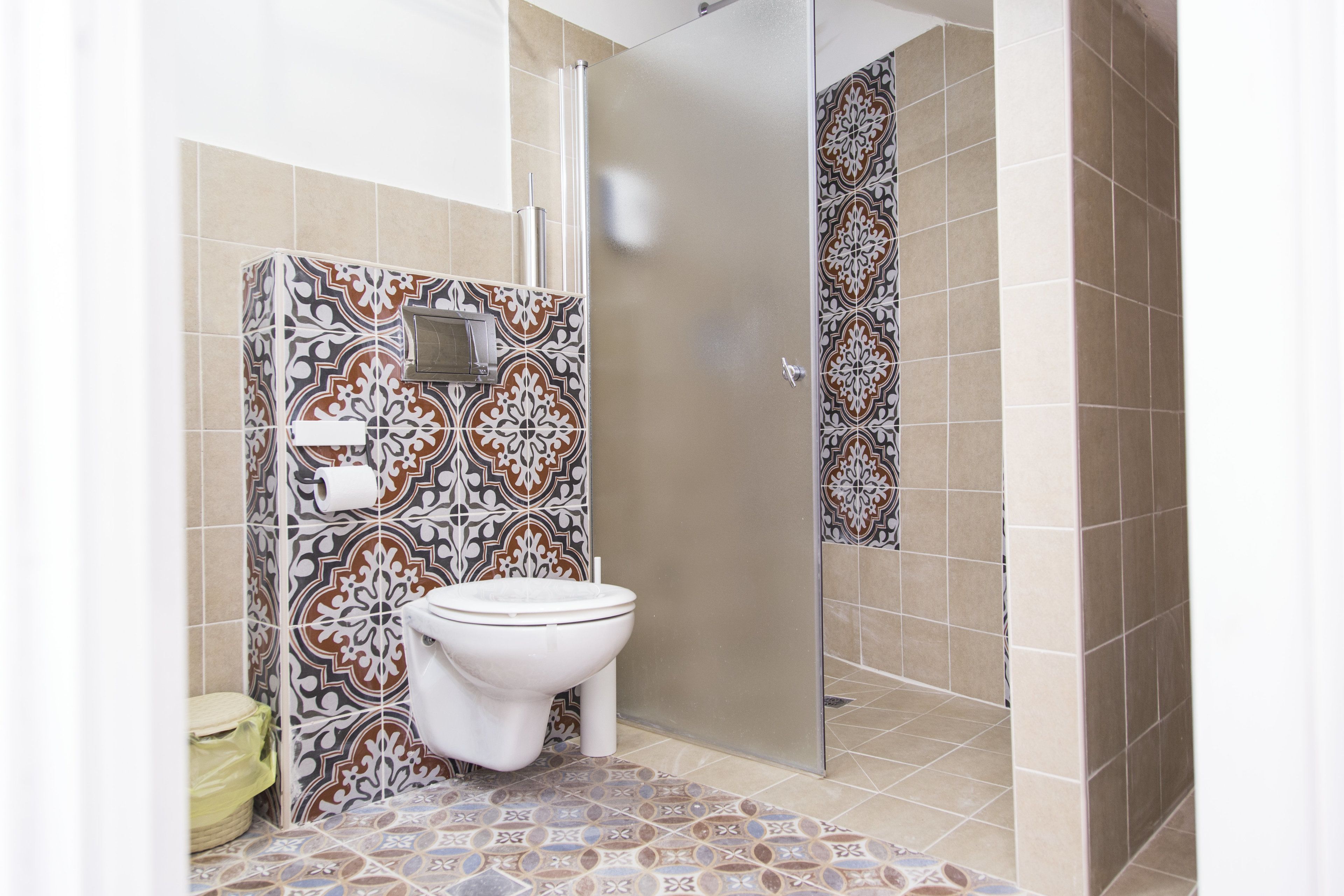 A bathroom with patterned tiles, a toilet, and a shower area.