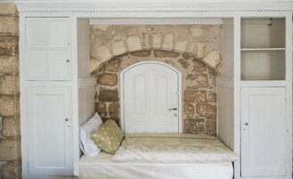 Una habitación con pared de piedra, puerta blanca y cama con ropa de cama estampada.