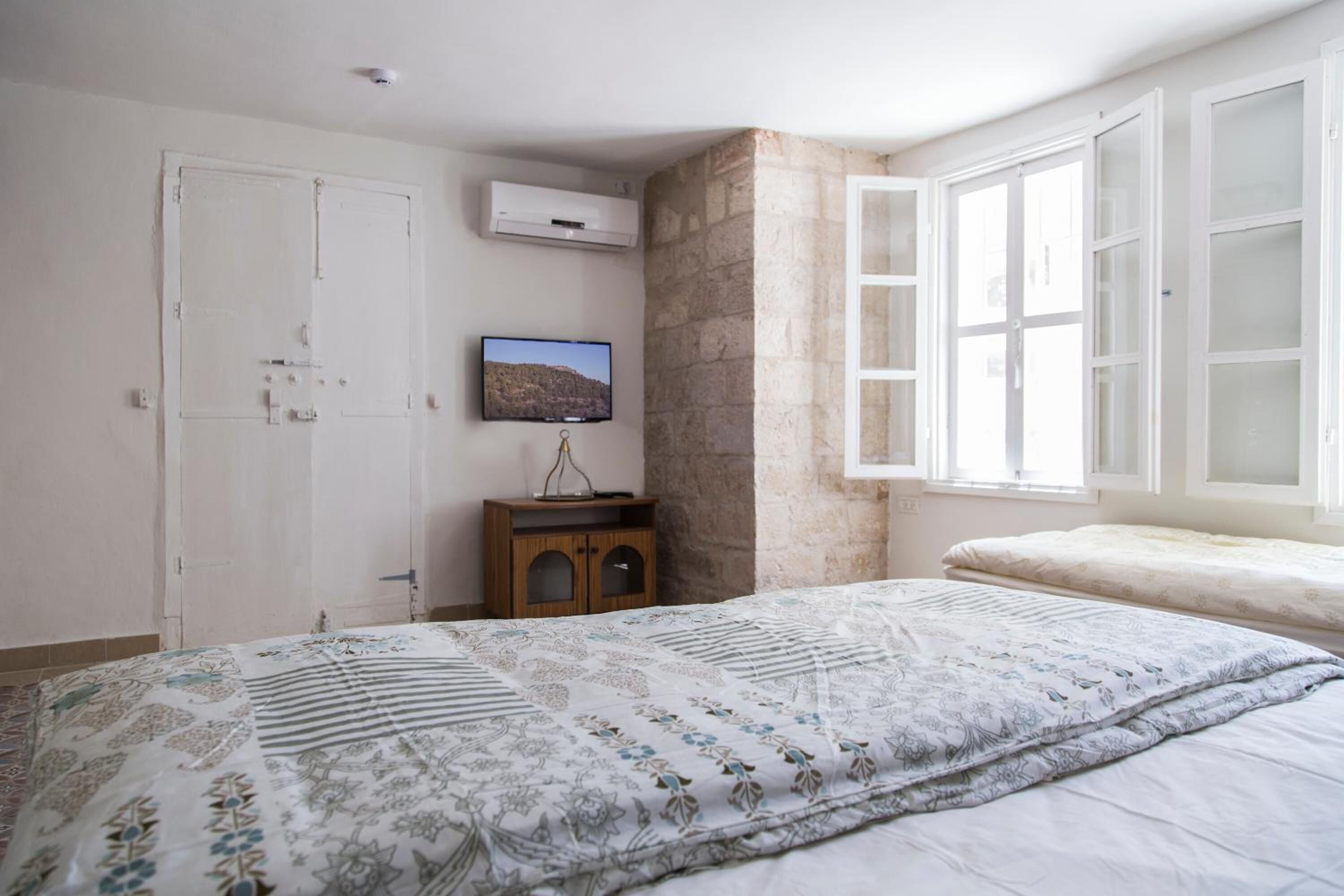 Un dormitorio con cama, televisor, armario y ventana con persianas abiertas.