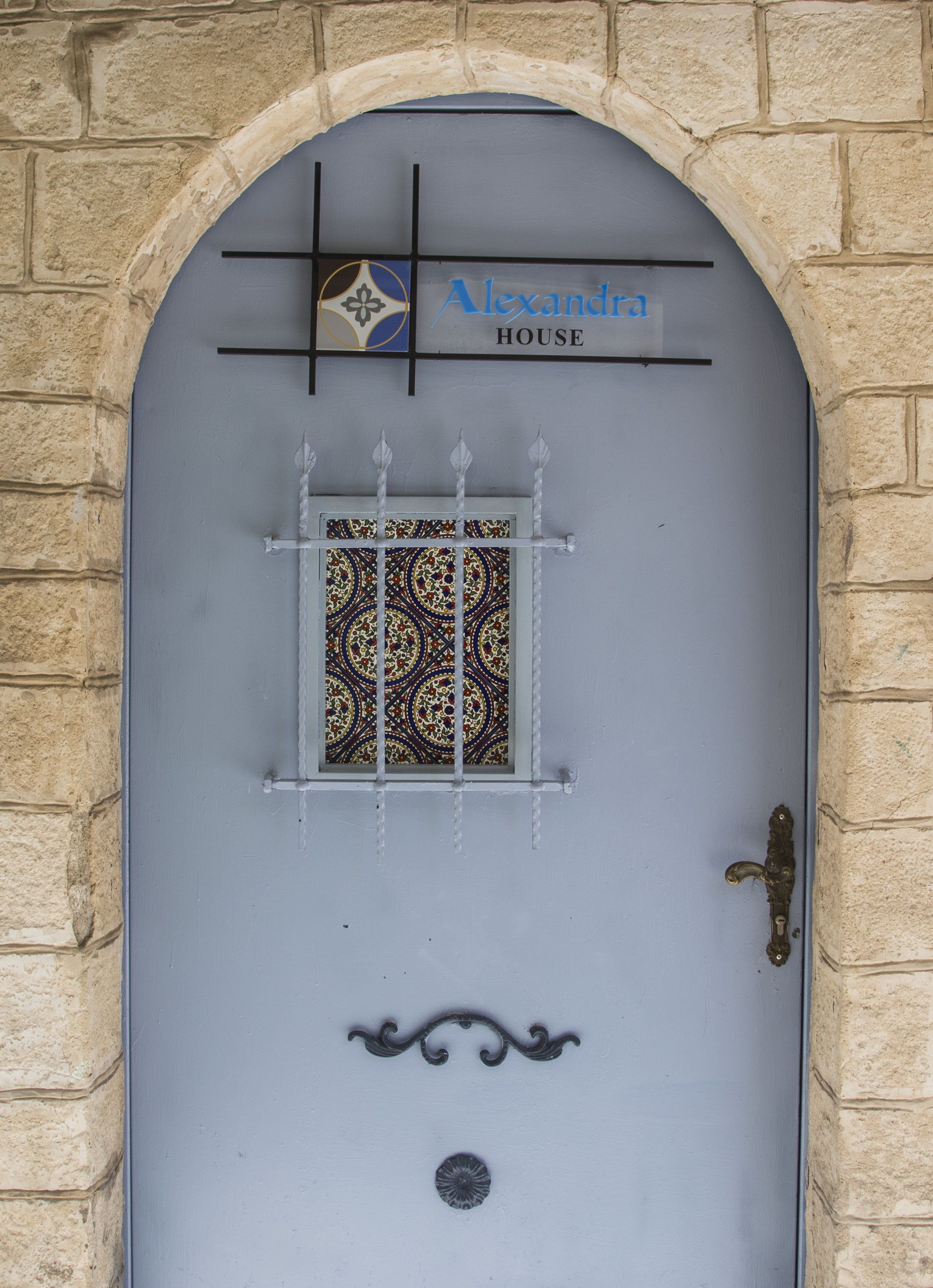 A blue door with a decorative window, a metal handle, and a sign above that reads "Alexandra House".