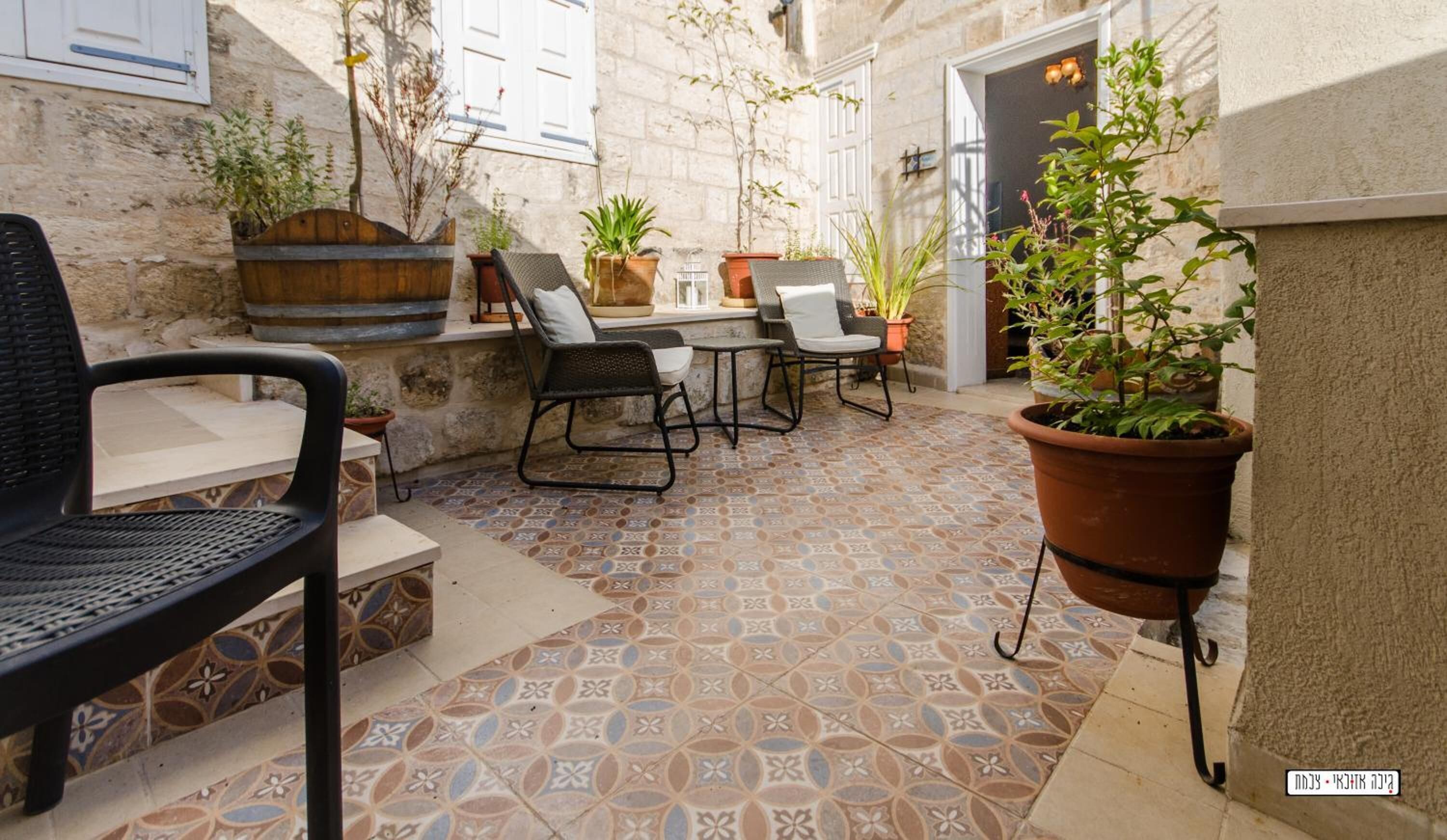 An outdoor patio area with tiled flooring, a stone wall, and several potted plants.