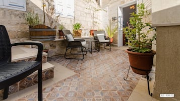 An outdoor patio area with tiled flooring, a stone wall, and several potted plants.