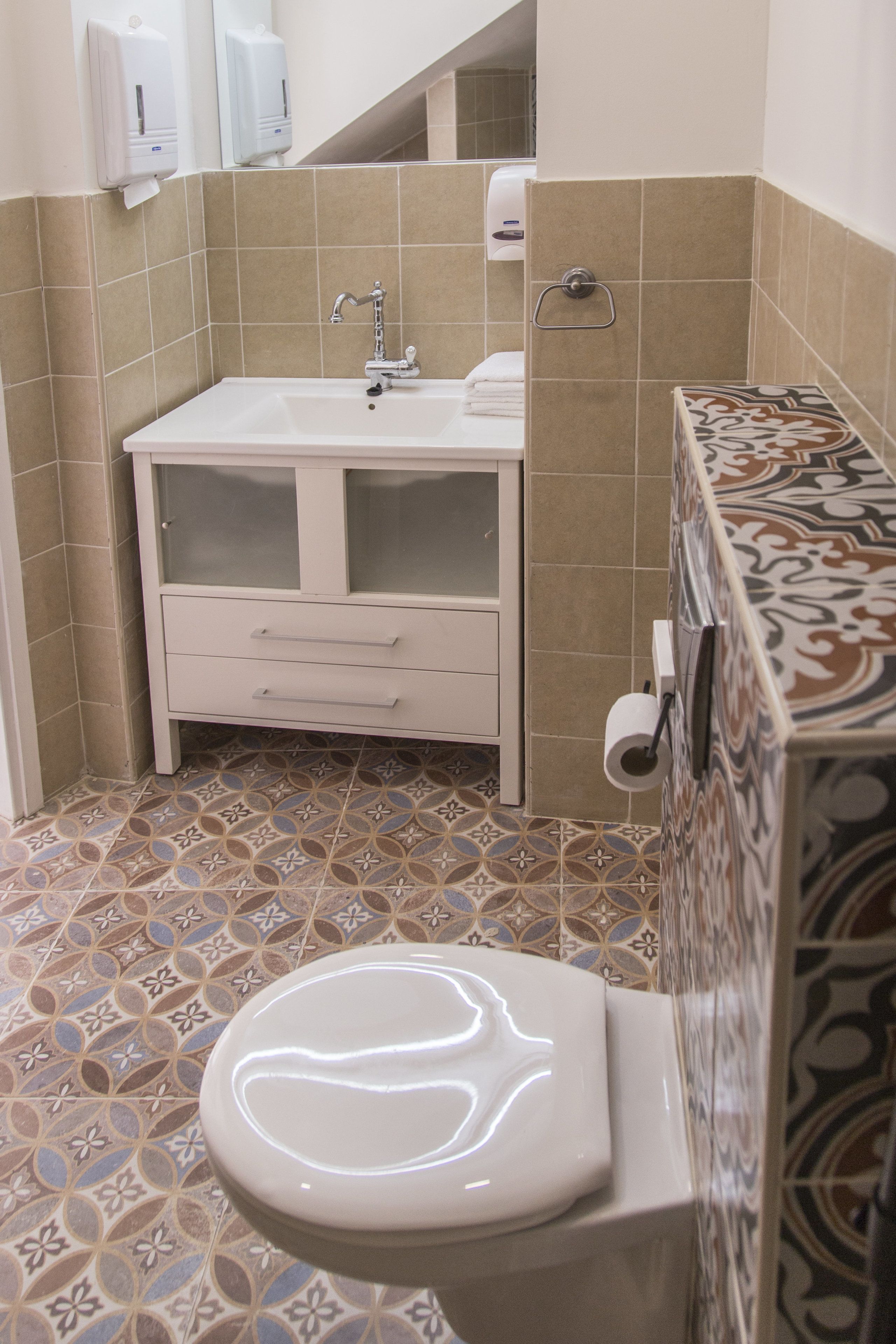 Un baño con un lavamanos blanco, un inodoro y baldosas estampadas en las paredes y el suelo.