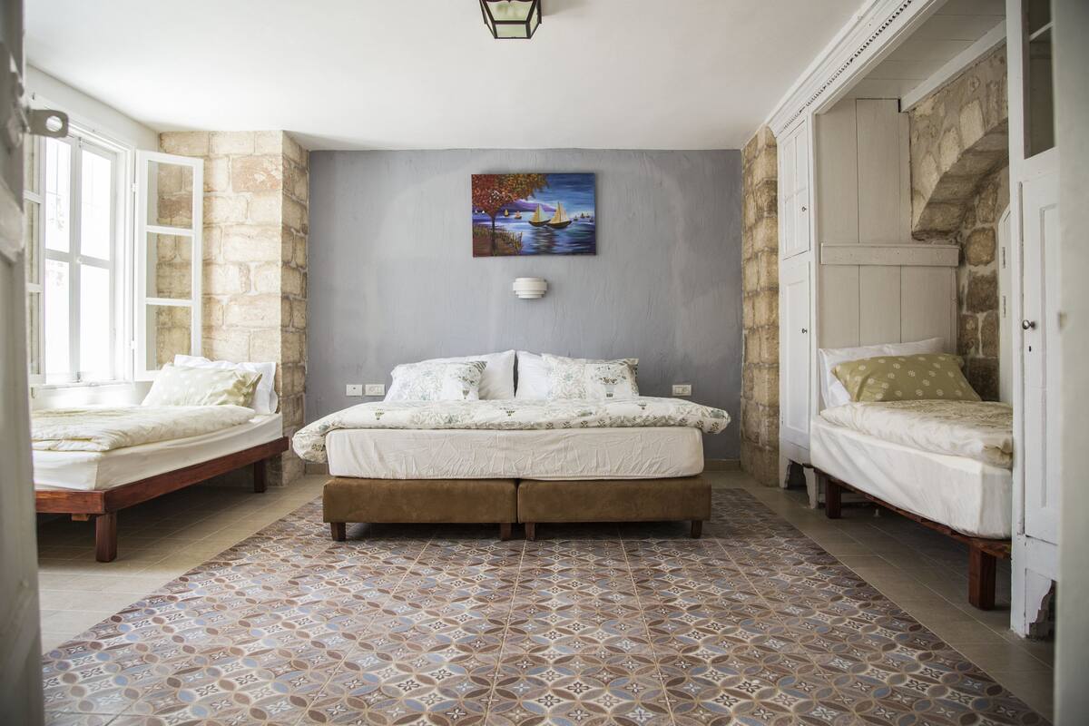 A bedroom with a large bed, two smaller beds, a patterned floor, and a painting on the wall.