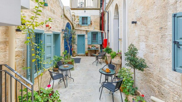 Un patio estrecho con paredes de piedra, contraventanas azules y mobiliario para exterior.