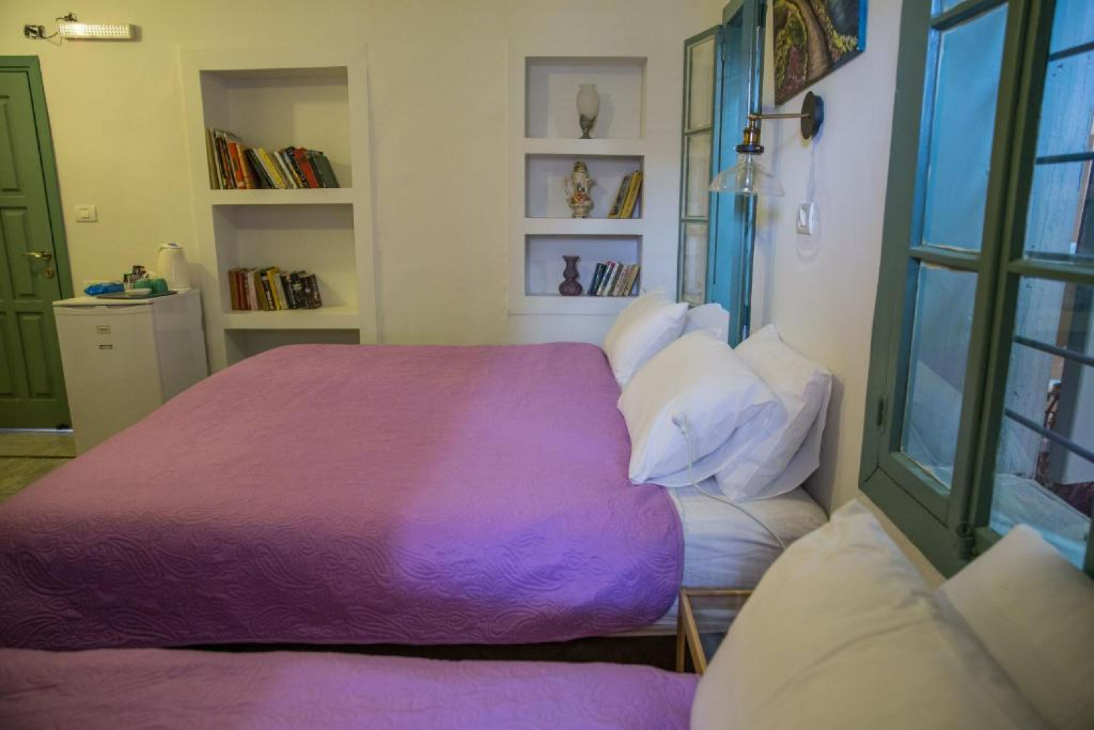 Une chambre avec deux lits, une bibliothèque et une fenêtre avec des volets bleus.