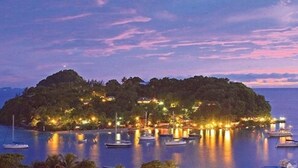 A coastal island with boats docked at the marina and buildings illuminated by lights. - Young Island Resort (Villa)