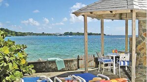 A seaside patio with lounge chairs and a table, overlooking the ocean. - Young Island Resort (Villa)