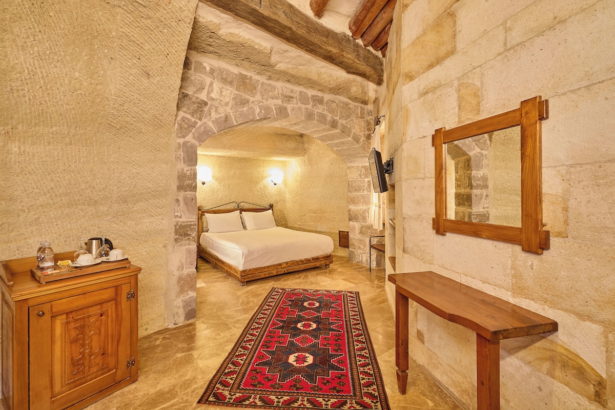A bedroom with a stone archway, a wooden bed, a bedside table, and a mirror on the wall.