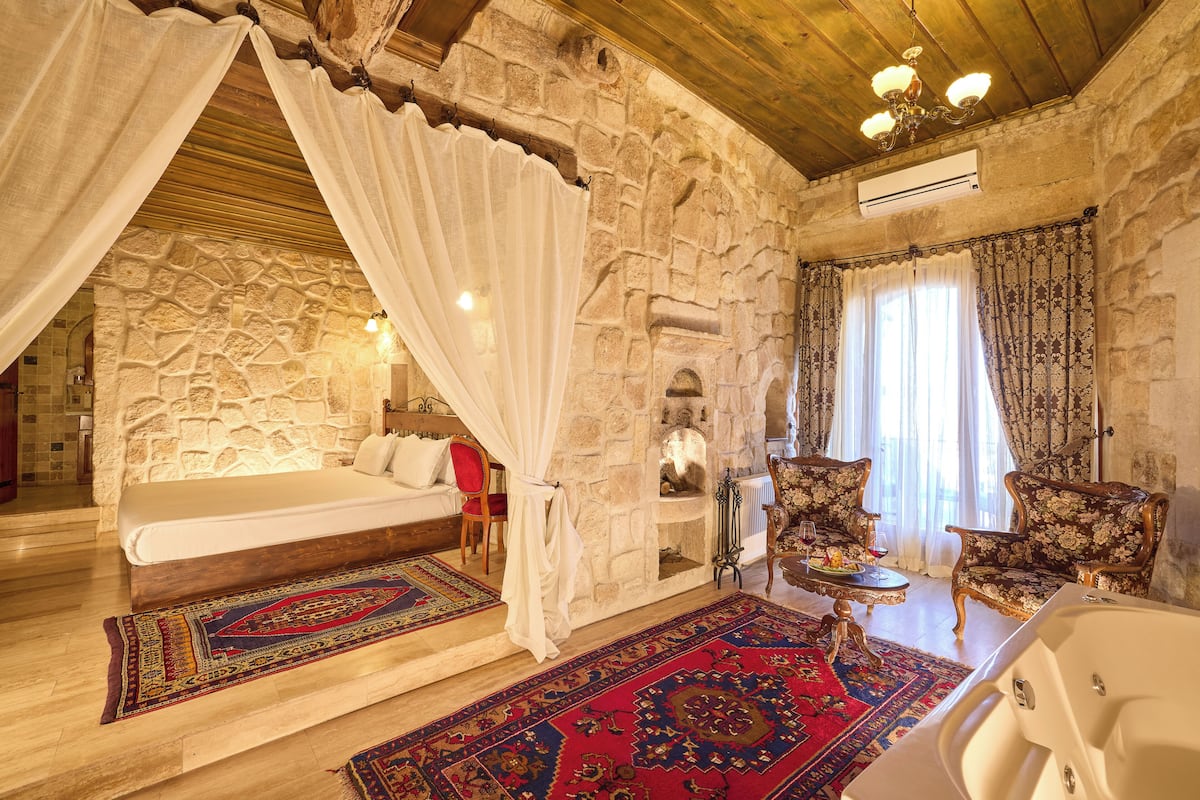 A stone-walled bedroom with a bed, a sitting area with chairs, a fireplace, and a bathtub.