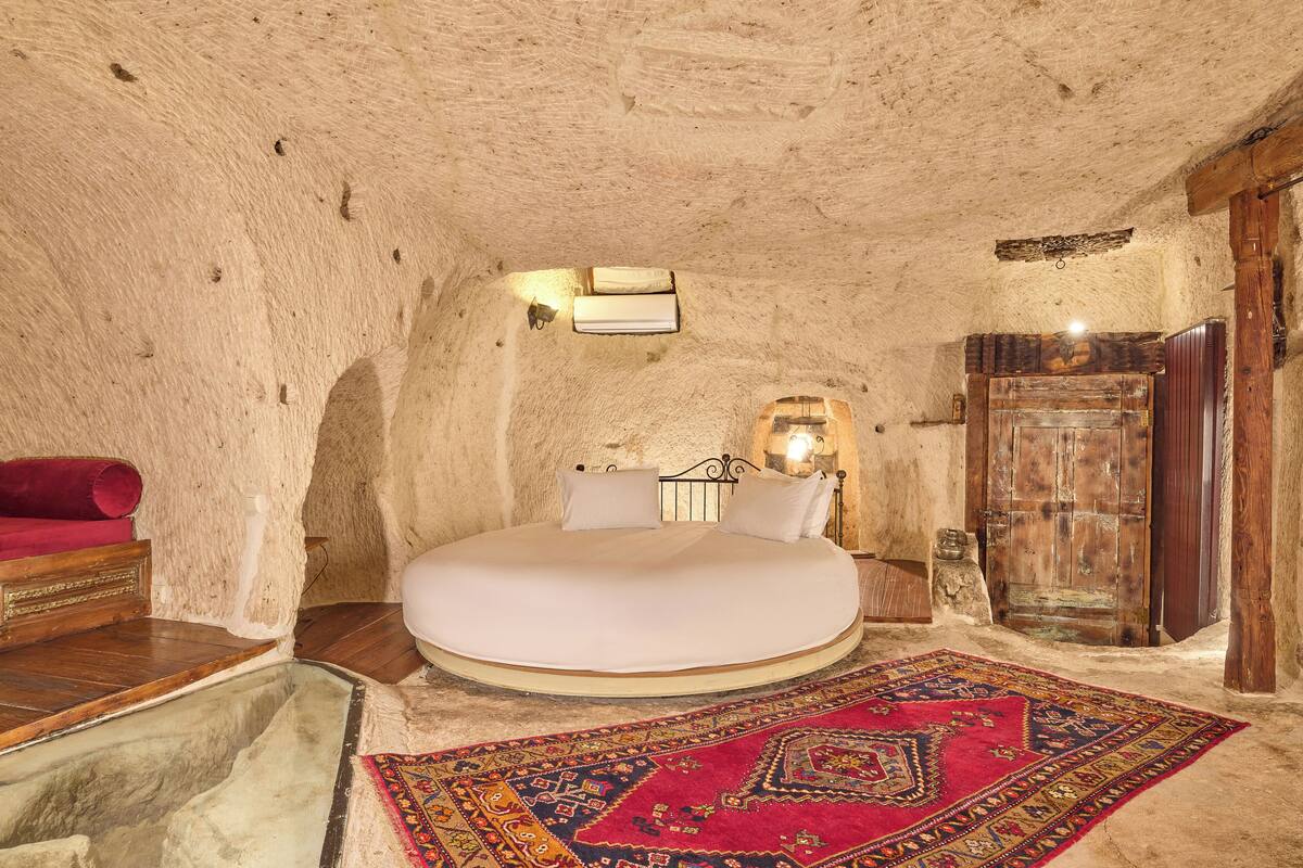 A circular room with a bed centered, a wooden door, and a red rug.