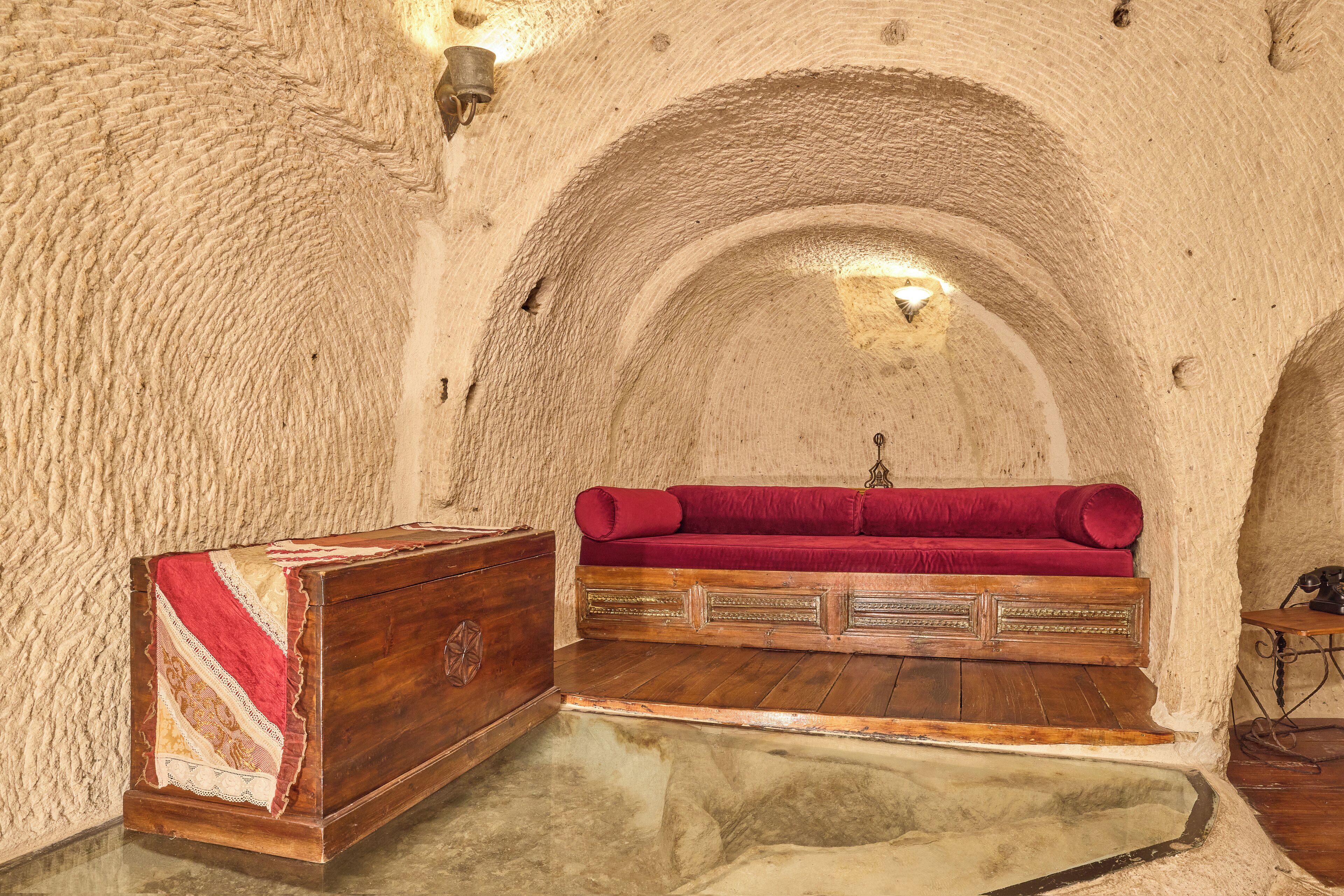 A room with a wooden chest, a red cushioned bench, and a stone wall.