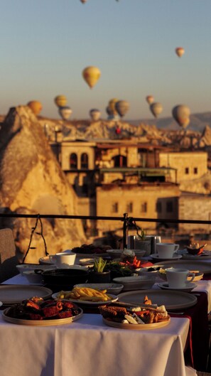 Una mesa servida con diferentes platos, con vistas a un pueblo de arquitectura tradicional y globos aerostáticos al fondo.