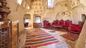 Una habitación con paredes de piedra, un aparador de madera, sillas tapizadas en rojo y una alfombra a rayas.